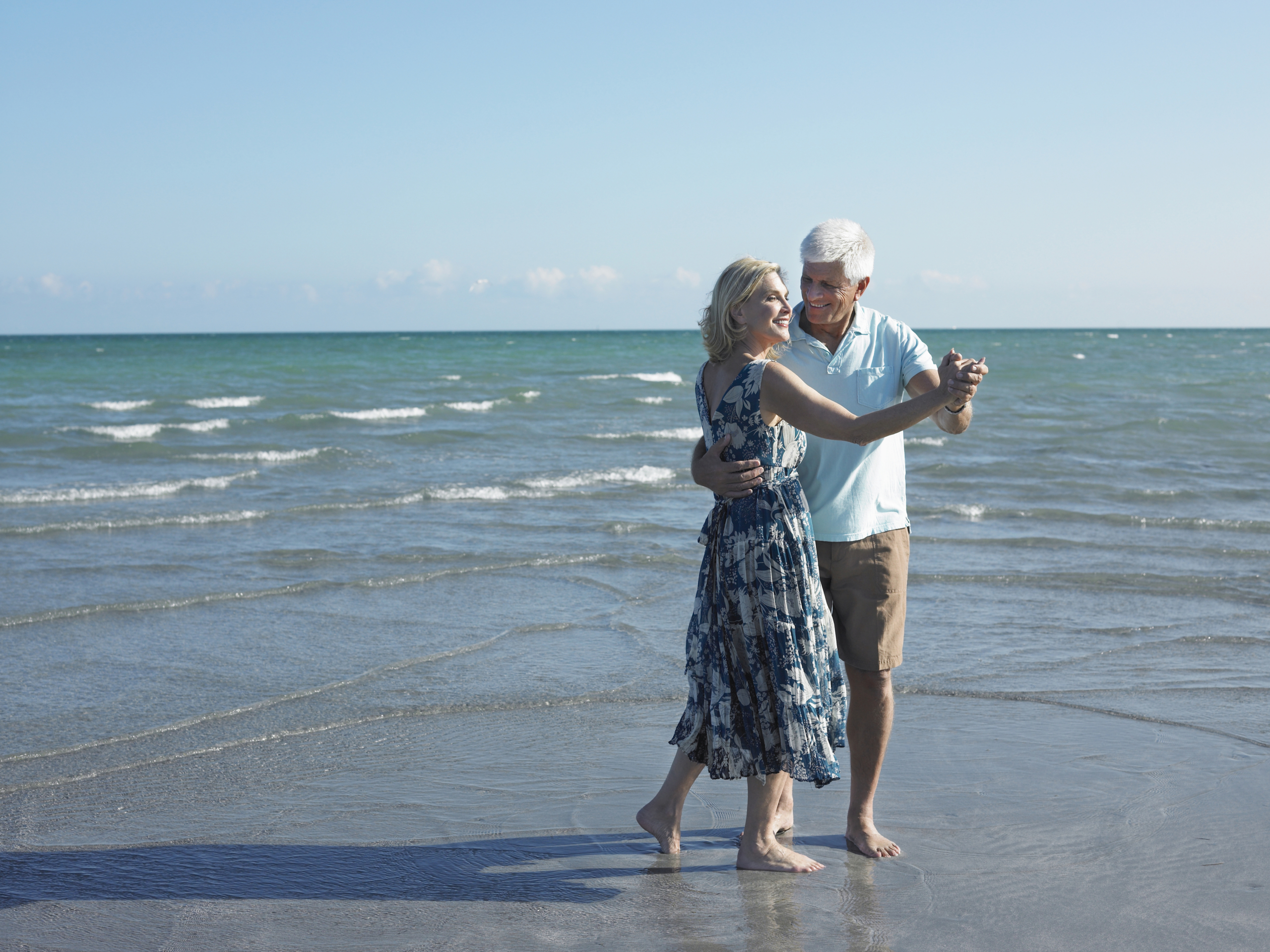 A couple in their 60s dancing on the beach and celebrating downsizing their home