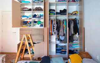 An image of a bedroom closet with open doors showing stacks of clothes that are ready to be organized.
