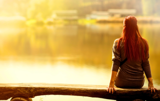 An image of a woman staring over a lake and reflecting on some life-changing events after she have decluttered her life.