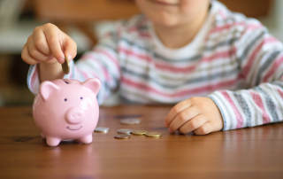 An image of a kid putting in her first savings on her piggy bank.