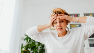 Woman in her 50s looking overwhelmed while standing in a cluttered home, illustrating emotional stress caused by clutter and failed organizing attempts.