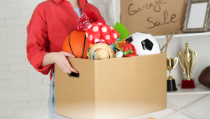 A woman holding a box filled with children’s toys and keepsakes while decluttering her home, symbolizing emotional decluttering and letting go of sentimental clutter.
