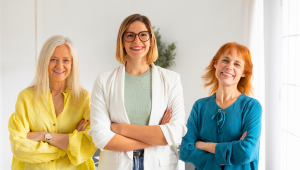 Three confident women of different ages standing side by side indoors with arms crossed and smiling, representing capable women navigating life transitions such as downsizing, decluttering, and intentional living.