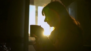 Silhouette of a woman holding a mug by a window in soft morning light, reflecting quietly on motherhood and life after her children have left home.