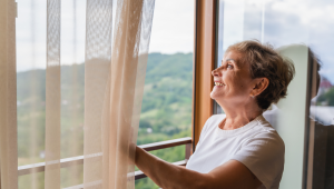 Woman standing by a window in soft morning light, reflecting on designing her life after the empty nest.