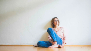 Mature woman sitting thoughtfully on the floor of an empty room, reflecting during a downsizing or life transition.