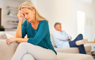 Midlife couple sitting apart in emotional distance, woman looking stressed and reflective during gray divorce or relationship transition.