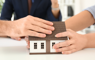Hands of adult family members holding a small model house together, symbolizing inheritance, homeownership, and generational decisions about property