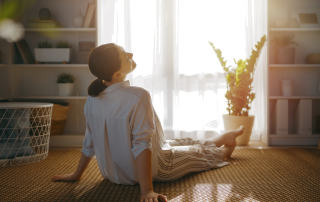 Woman sitting peacefully on the floor in a bright, clutter-free room, surrounded by natural light, plants, and simple home décor, symbolizing calm, intentional living, and reclaiming your space.