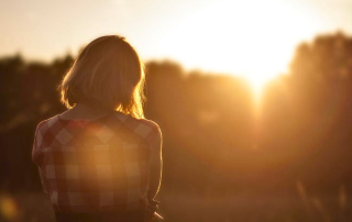 Woman in her 60s looking at sunrise, reflecting on new beginnings and life after retirement.