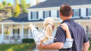 Couple standing together looking at their large home, reflecting on downsizing and life transition decisions.