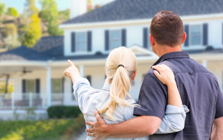 Couple standing together looking at their large home, reflecting on downsizing and life transition decisions.