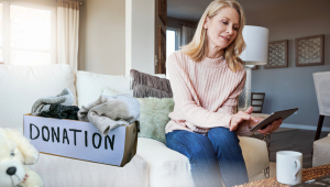 Woman sitting on a couch with a tablet beside a donation box filled with clothing, reflecting on decluttering and letting go without regret.