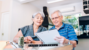 Older couple reviewing retirement plans together at a table with savings, paperwork, and happy retirement blocks, reflecting the lifestyle and financial decisions of retirement.