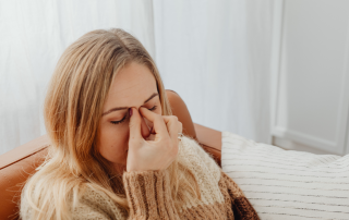 Woman sitting on a couch with her eyes closed, gently pinching the bridge of her nose, looking overwhelmed and stressed while decluttering.